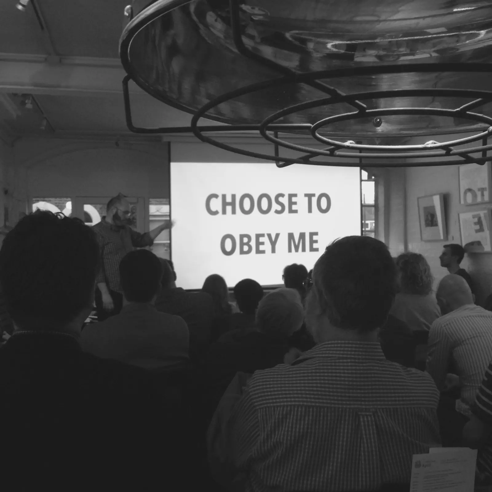 Glyn Cannon giving a talk to an audience in front of a large caption that reads 'Choose To Obey Me'